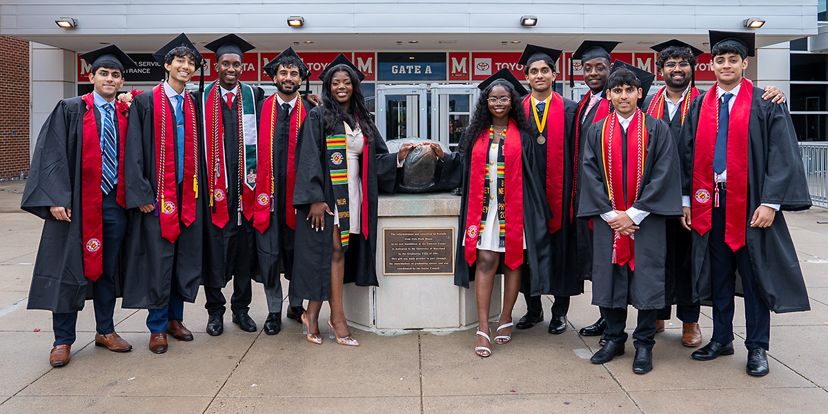 A group undergraduate students, wearing commencement regalia, flanking the bronze Testudo outside of the Comcast Center. Credit: Mark Sherwood.