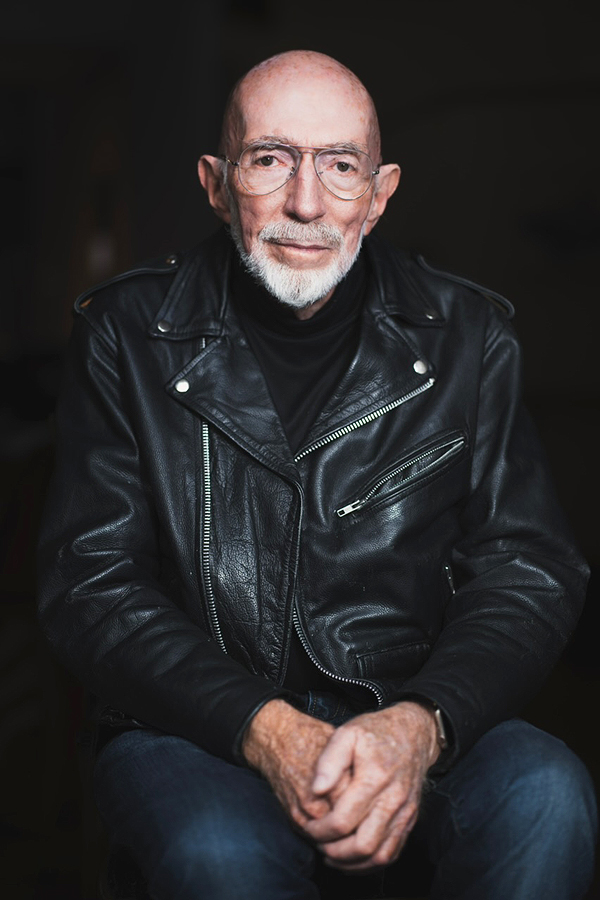 Kip Thorne wearing a leather biker jacket and jeans, against a black background. Credit: Christopher Michel.