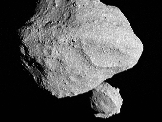 A black and white photo of a tiny, lumpy moon orbiting an asteroid. Credit: NASA Goddard/SWRI/Johns Hopkins APL/NOAO.