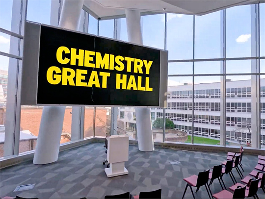 A video still from a drone flying through the new Chemistry Wing 1's Great Hall, a lecture space with a huge screen and expansive views of campus.