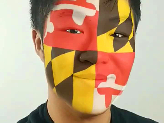 Screen capture of a young Asian man with a Maryland flag pattern applied to his face like facepaint