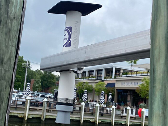 One of the flooding sensors mounted on a dock in Annapolis, Maryland. The sensor looks like a large greyish-white tube with a small flat room on top.