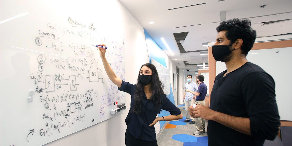 A woman and a man at a whiteboard. THe woman is drawing figures and writing equations.