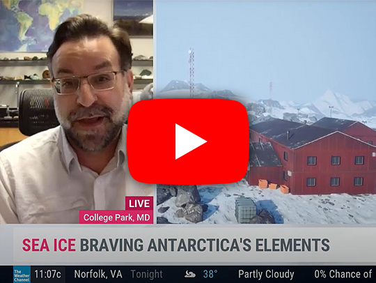A split-screen video still from the Weather Channel showing Nick Schmerr on the left and a red barn-like station in Antarctica on the right. This image is linked to the video.