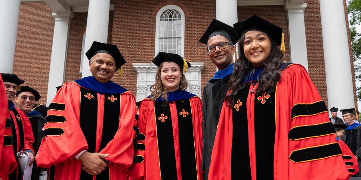 A group of graduate students and faculty at commencement, wearing regalia, on the patio of the UMD Chapel. Credit: Mark Sherwood.