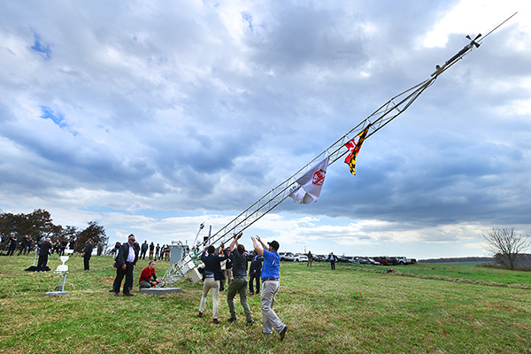 A research team raising a Mesonet tower in a field on a cloudy day.