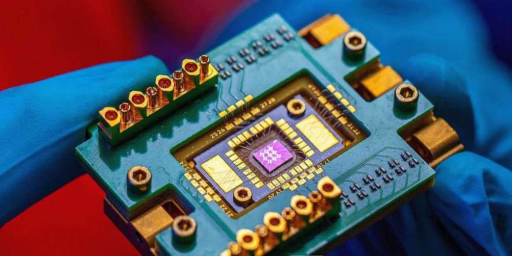 Close-up of a quantum computing component small enough to be held between the finger and thumb of a blue-gloved hand.