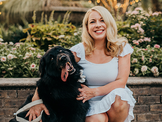 Lynsey White in a garden, kneeling beside a large black dog