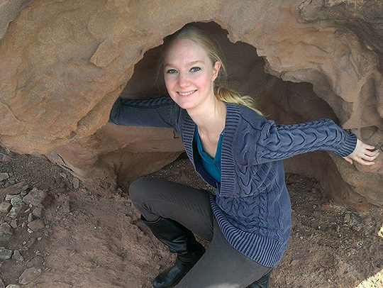 Shauna Rashband kneeling in a cave entrance.