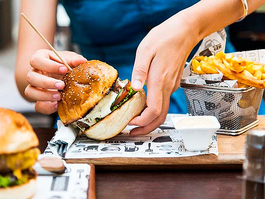 Hands holding a thick, delicious-looking hamburger, with a bowl of fries sitting to the side. Credit: Healthday