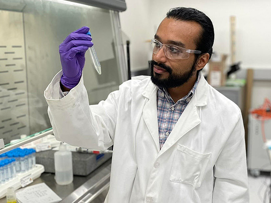 George Caceres in a lab, wearing a white lab coat and blue gloves. Credit: M.King, NIST.