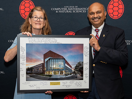 Janice Reutt Roby with Amitabh Varshney at a leadership recognition dinner, holding a large framed photo of the new Chemistry Wing 1 building.