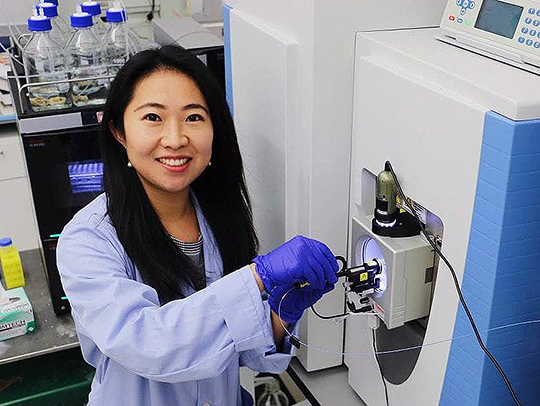 Ling Hao in her lab, standing at a piece of equipment. She is wearing a light blue lab coat and purple gloves/ Credit: Mark Sherwood.