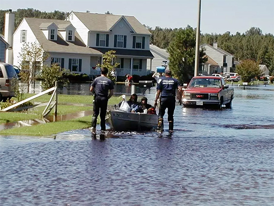 A flooded suburban neighborhood on the Chesapeake Bay. Two rescue workers are pulling a boat containing 3 people down a flooded street. Credit: U.S. Fish and Wildlife Service.