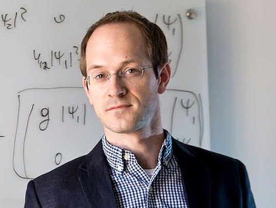 Andrew Childs in front of a whiteboard with equations written on it.