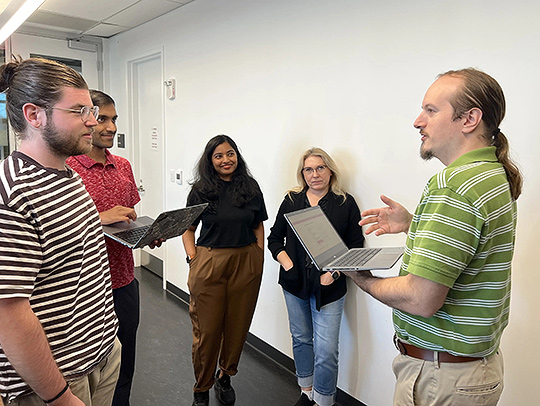 Matthew Baney holding a laptop while talking to a group of students