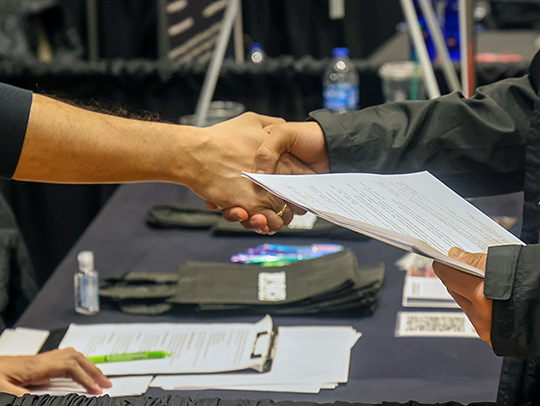A photos of two men shaking hands. one is holding a resume.