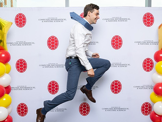 A male student leaping into the air at the departmental commencement celebration