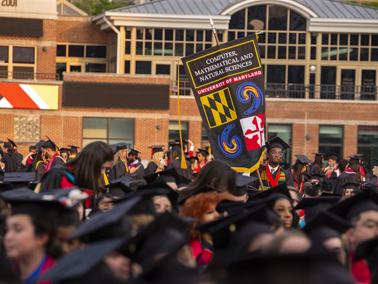 The Computer Science senior marshals amidst the crowd at UMD's main commencement ceremony, holding the Computer Science Banner