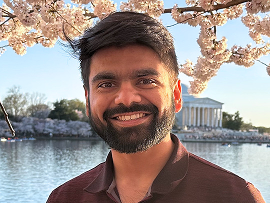 Sreyan Ghosh outside in Washington, D.c. with cherry blossoms and water in the background.