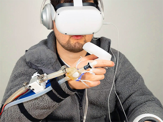 A young man with a beard wearing VR goggles and haptic feedback gear on his hand.