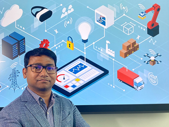 Nirupam Roy stading in front of wall art depicting computers, tablets, headsets and circuits