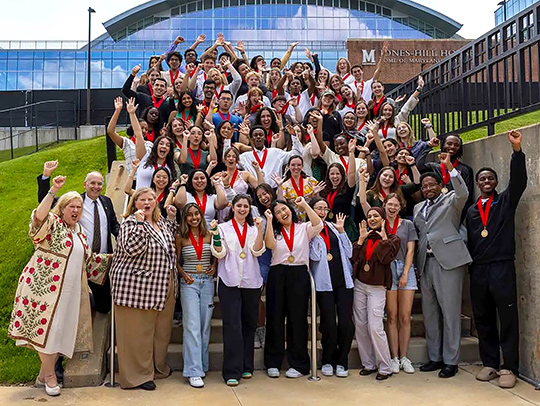 A photo of the large group of students selected to serve as Senior Marshals. They are standing on steps outside of the stadium. Credit: John T. Consoli.