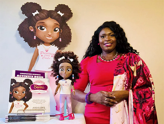 Bukola Somide standing beside a Somi doll and a stack of Somi books