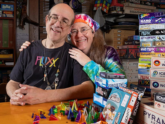 Andy and Kristin Looney sitting together at a table bearing stacks of their games.