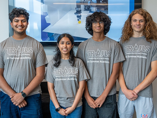 A group of students at the TRAILS AI summer school. Each is wearing a T shirt withthe TRAILS logo on it.