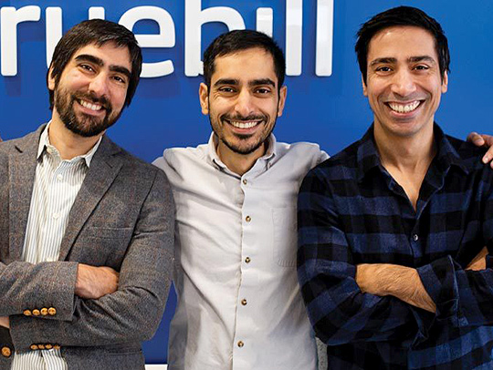 Truebill founders standing in front of a wall with the company logo on it
