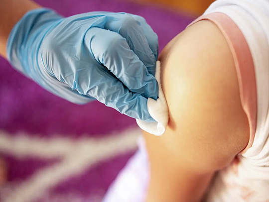 A gloved hand wiping a shoulder with an alcohol pad in preparation of administering a shot. Credit: iStock