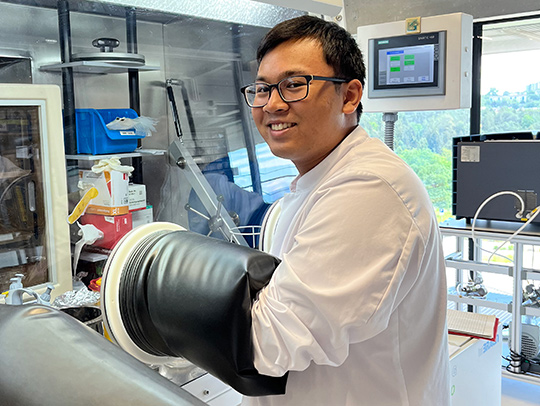 Garmani Thein, wearing a lab coat and working at a glovebox