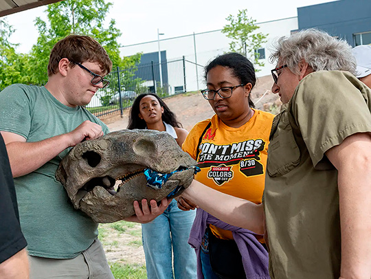 Liam Driver '27 holds a model fossil head of a Priconodon, an armored dinosaur that could grow up to 45 feet long. A group of three women look on. Liam Driver '27 holds a model fossil head of a Priconodon, an armored dinosaur that could grow up to 45 feet long. A group of three women look on.