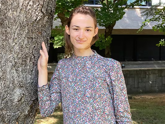 Hannah Cairo standing outside with her arm resting on a tree trunk.