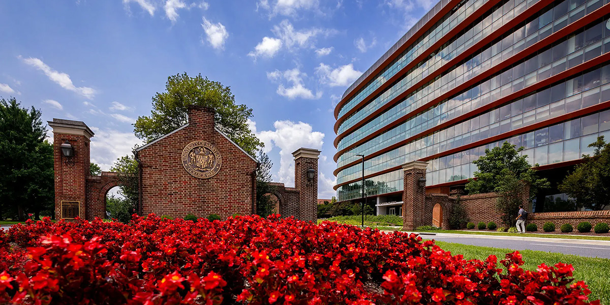 The brick North Gate of the UMD campus with red flowers in the foreground and the Iribe Center in the Background. Credit: John T. Consoli.
