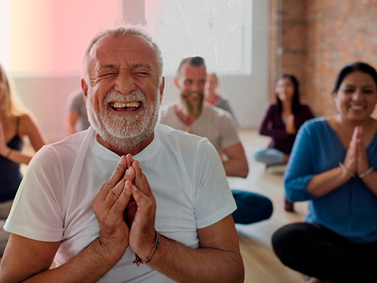 A yoga class for seniors. A smiling man with a white beard is in the foreground. Credit: AdobeStock