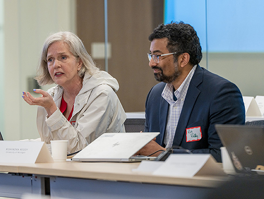 A silver-haired woman and a bearded man sitting at a table at the healthcare summit.