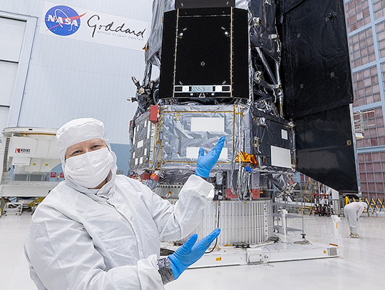 Jackie Townsend at NASA Goiddard. She's wearing a clean room suit and gesturing toward the Nancy Grace Roman Space Telescope mission.