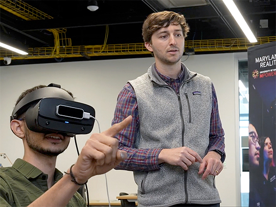 Jonathan Hagerty, standing alongside a seated male student who is wearing a VR headset and pointing. Credit: Mark Sherwood.