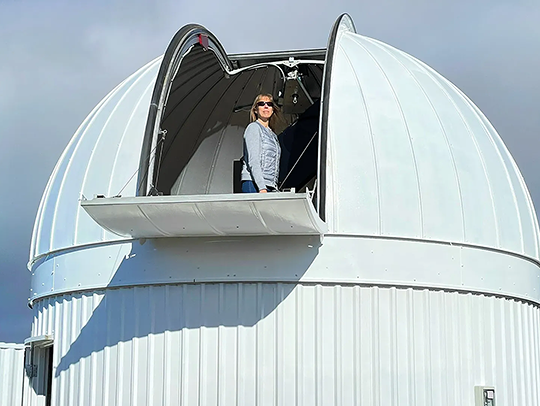 Kelly Fast standing at the top of the open dome of an observatory.