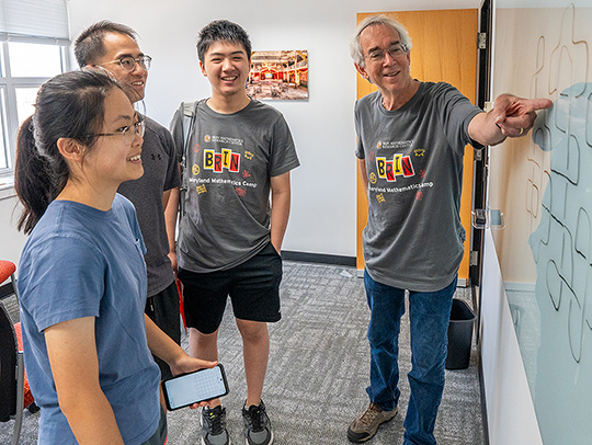 Lawrence Washington showing something to three students at a whiteboard. Everyone is smiling.