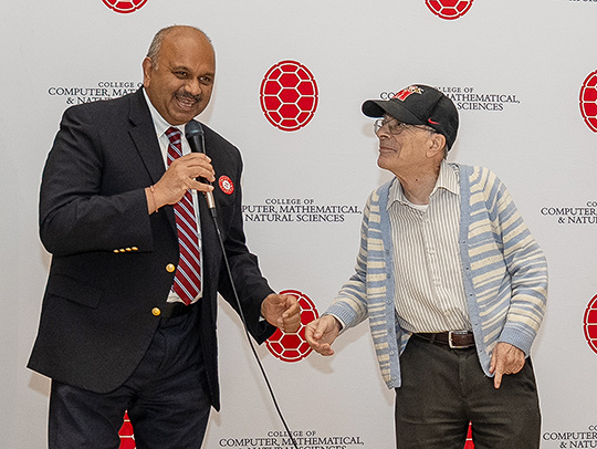 Dean Amitabh Varshney and Professor Emeritus Danny Gulick joking around in front of a backdrop with shell logos on it. Credit: Mark Sherwood.