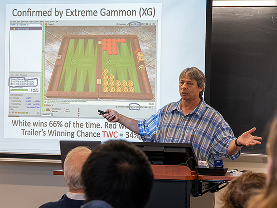 Arthur Benjamin giving a lecture about the math behind backgammon. A slide showing a backgammon board is behind him. Credit: Mark Sherwood.