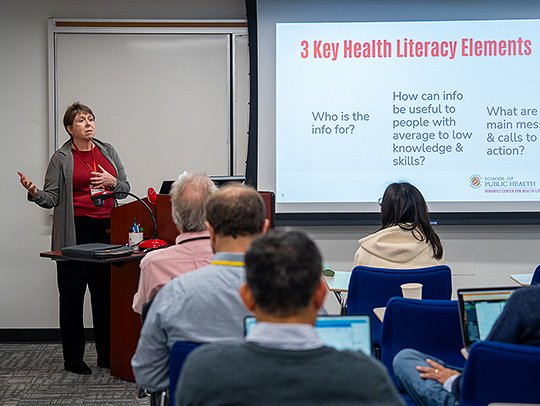 Cynthia Baur giving a presentation at one of the many Brin Workshops held in 2024. A slide on the screen is titles, 3 Key Health Literacy Elements. Credit: Mark Sherwood