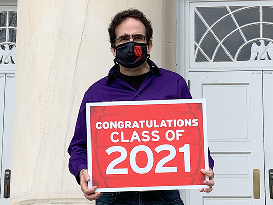 Doron Levy wearing a mask and holding a sign congratulating the Class of 2021