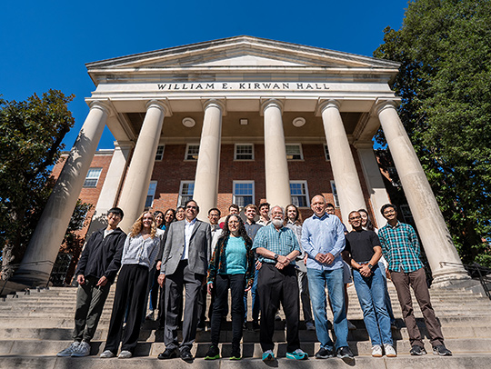 A large group of faculty and students on the steps of Kirwin Hall with donors Carol Fullerton and James A. Yorke after celebrating the Fall 2024 Haptman Fellowship awardees.