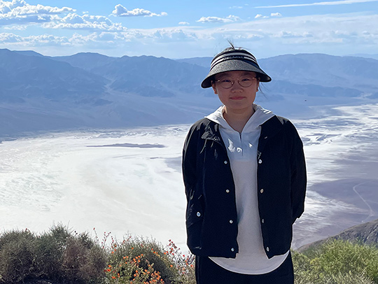 Mengting Chao stading at an overlook with a beautiful mountain range in the background