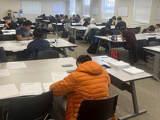 Students working on match problems, seated at long tables at the Putnam competition