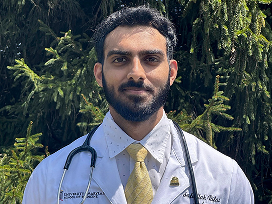 Safiullah Rifai wearing a white doctor's coat with the University of Maryland logo on it. A stethescope is around his neck.